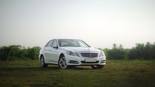 Free White sedan parked in a green field with trees under a clear sky, showcasing rural serenity. Stock Photo