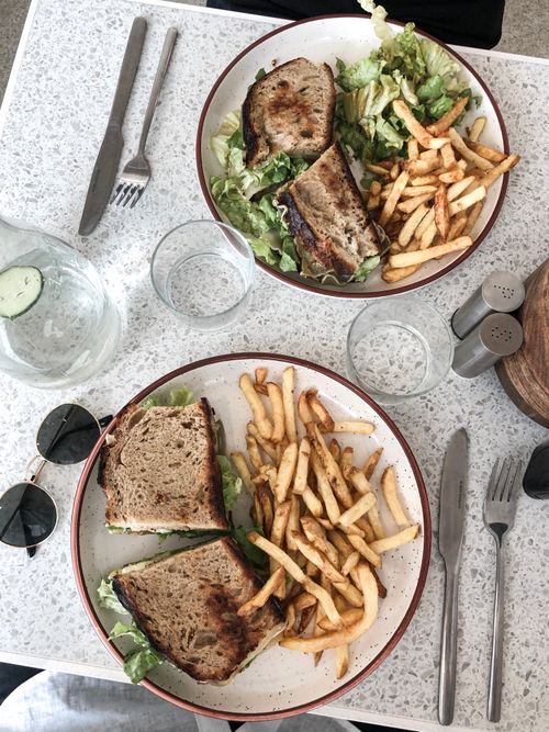 Free Two plates with sandwiches, fries, and salad viewed from above, illustrating a casual restaurant meal. Stock Photo
