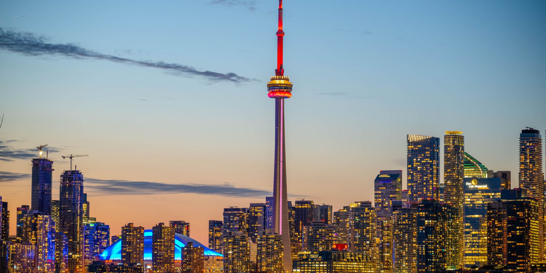 Beautiful sunset view of Toronto skyline with CN Tower and city lights reflecting on the lake.