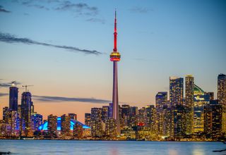 Beautiful sunset view of Toronto skyline with CN Tower and city lights reflecting on the lake.