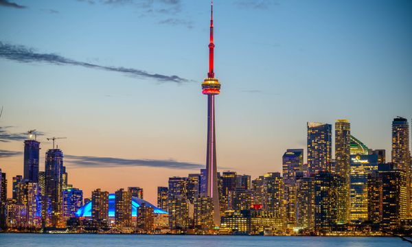 Beautiful sunset view of Toronto skyline with CN Tower and city lights reflecting on the lake.