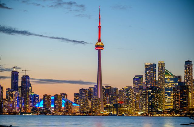 Beautiful sunset view of Toronto skyline with CN Tower and city lights reflecting on the lake. — arriving in Toronto