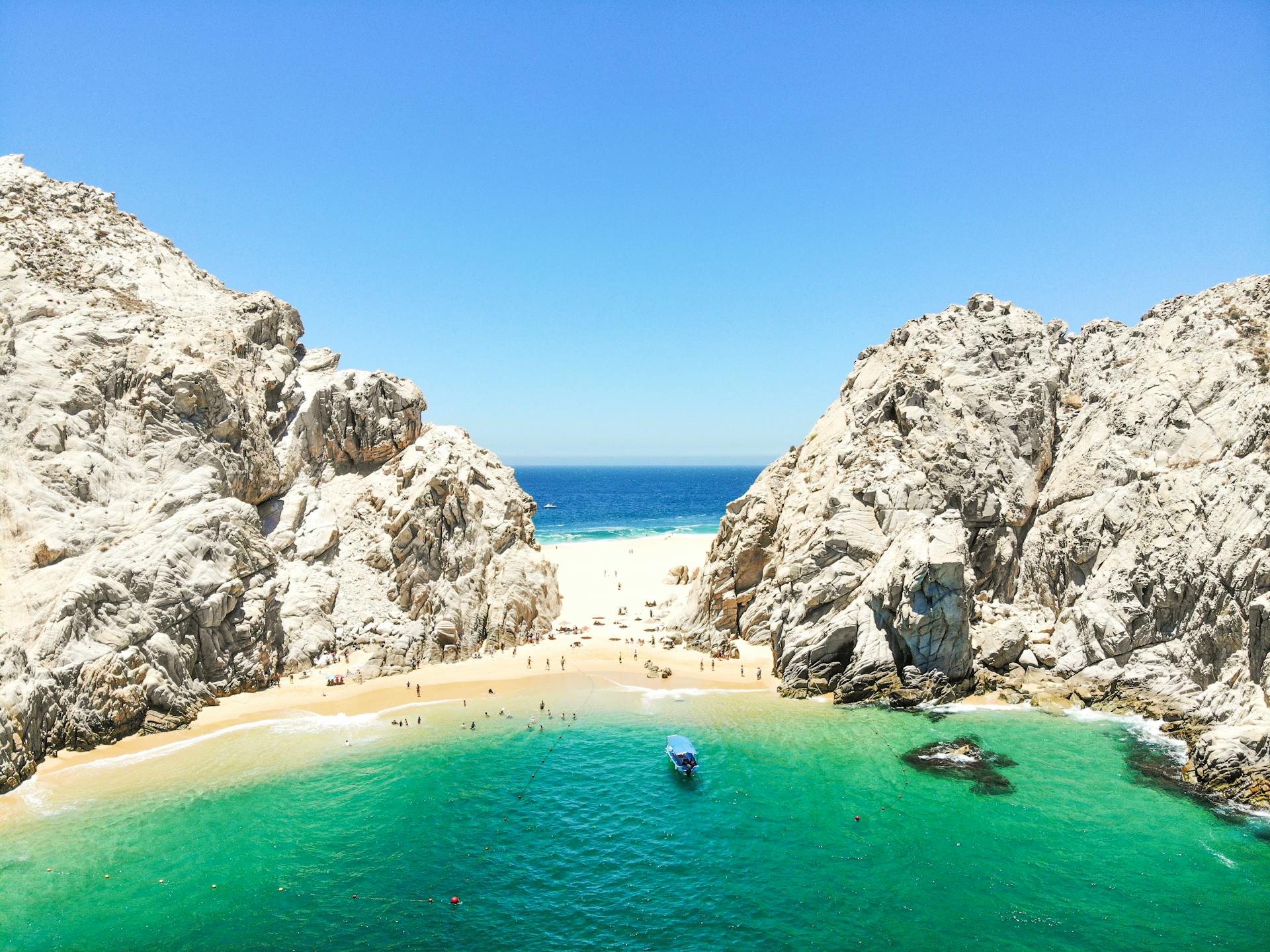 Discover a breathtaking aerial view of a secluded beach cove surrounded by rocky cliffs under a clear blue sky.