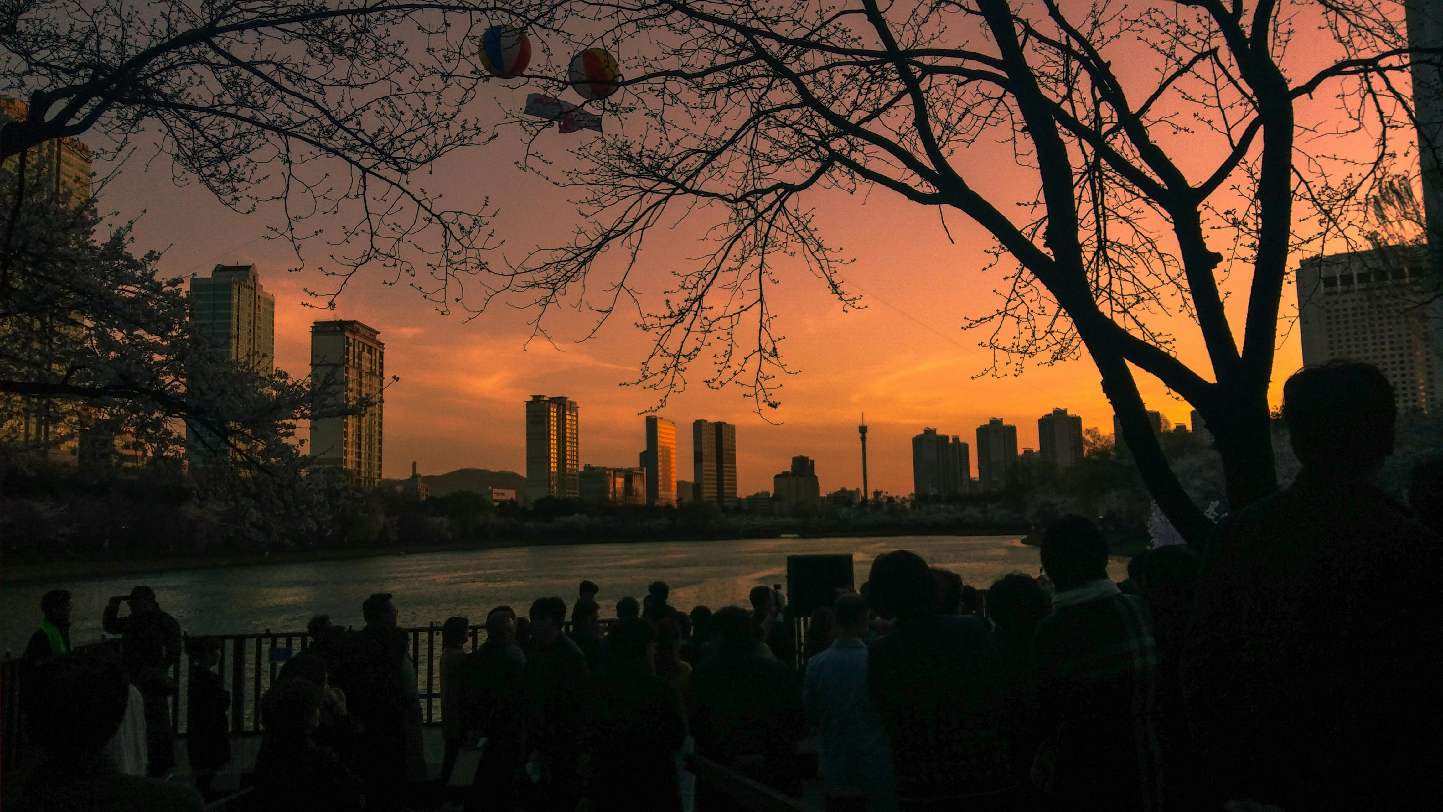 日落时分，河边的人群轮廓映衬着首尔的天际线
