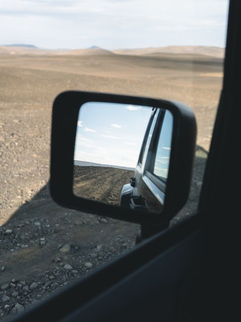 View of Iceland's rugged terrain reflected in a car side mirror, evoking a sense of adventure.