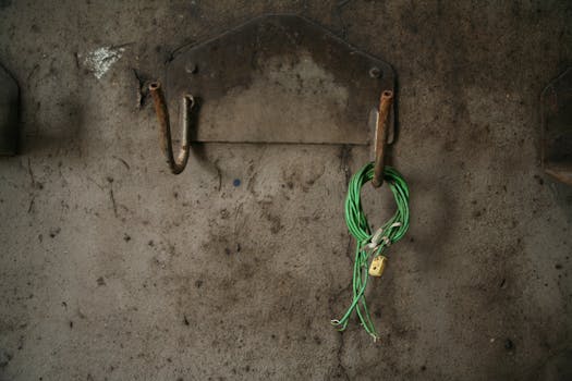Green wire loop with padlock hanging on a rustic, rusty wall hook.
