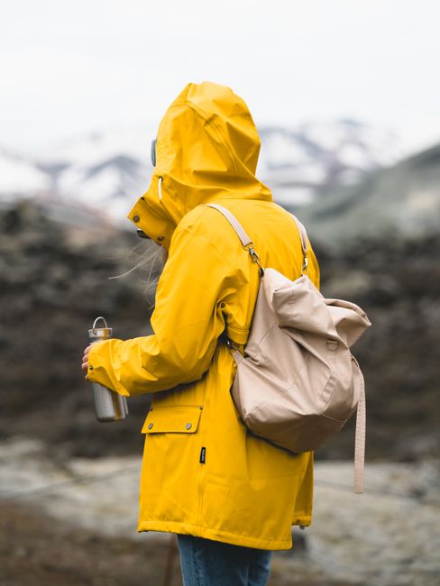 Person in a yellow raincoat exploring Iceland's rugged terrain with a backpack.