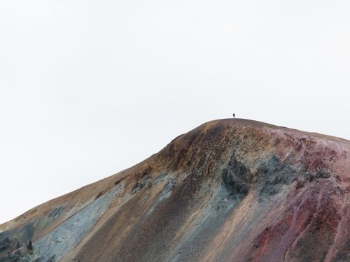 Free A lone hiker stands atop a colorful mountain in Iceland, showcasing stunning natural beauty and solitude. Stock Photo