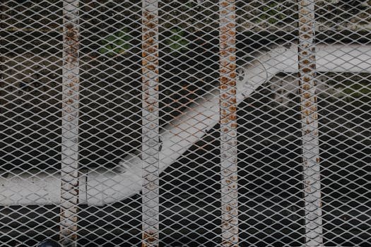 Close-up view of a rusty metal grid with a pipe in the background, showcasing industrial textures.