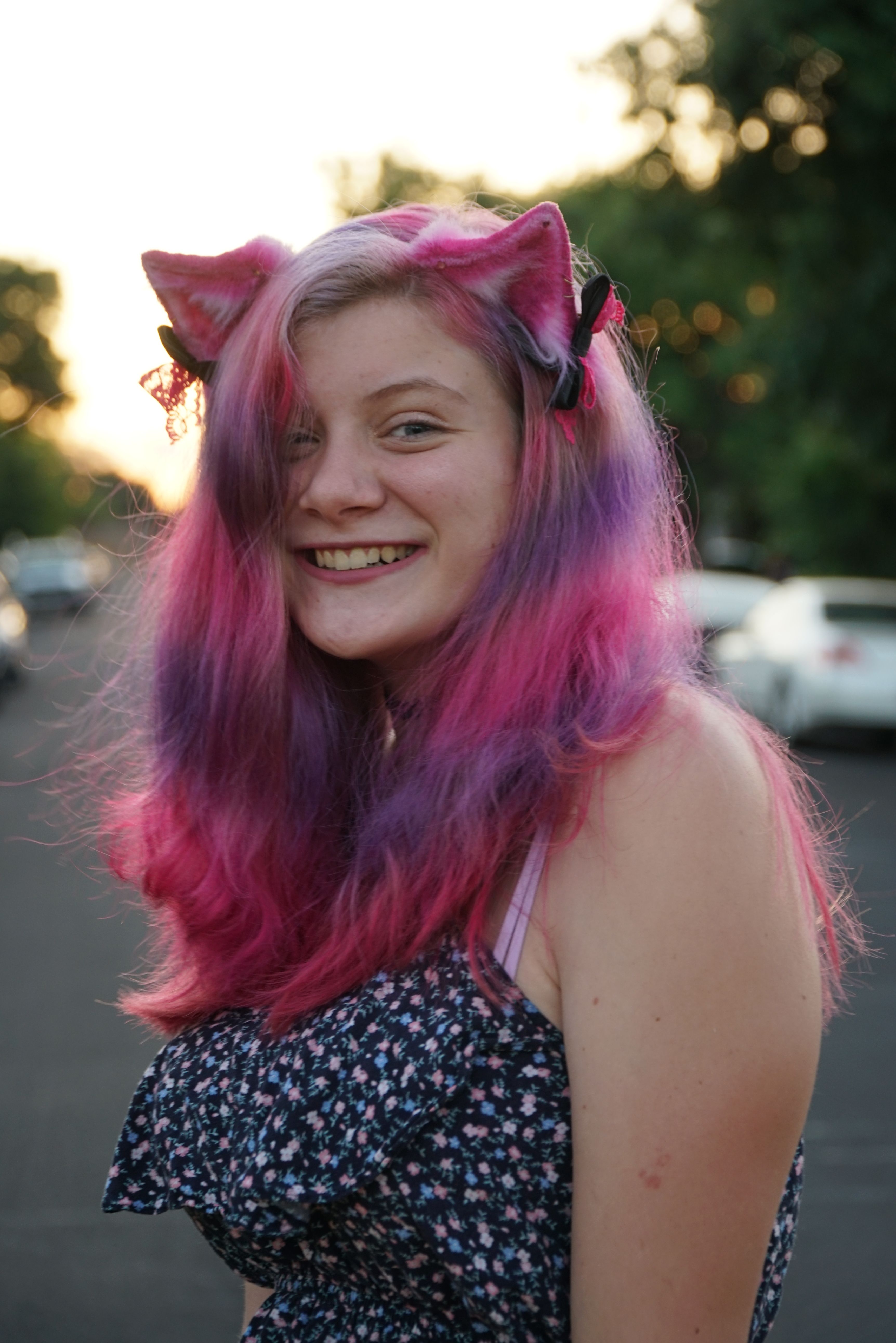 Happy woman with vibrant pink hair smiling outdoors at sunset.