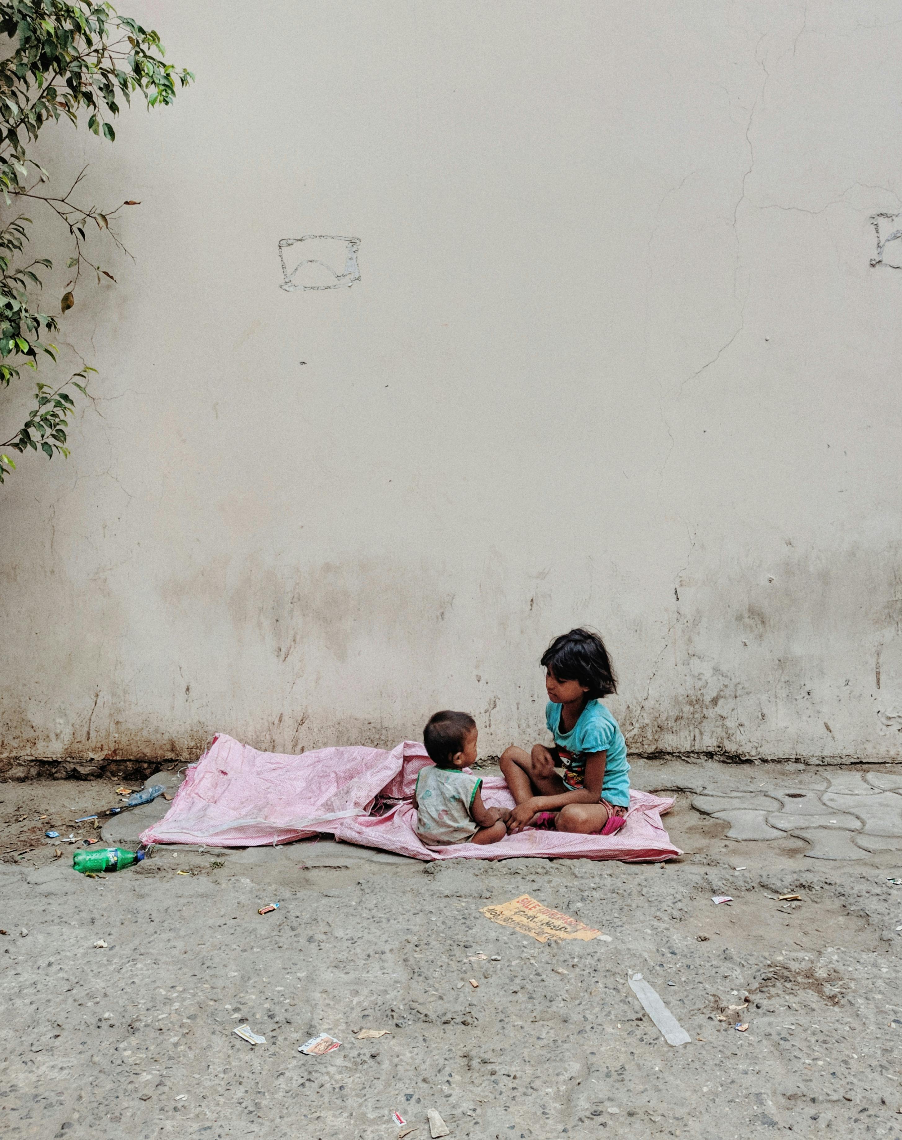 在印度诺伊达，两个孩子坐在人行道上，裹着毯子，构成了一个坦率的街头瞬间
