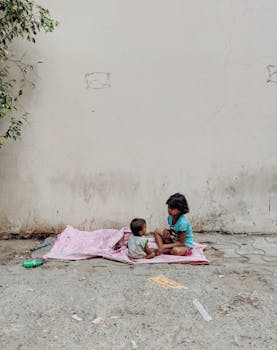 在印度诺伊达，两个孩子坐在人行道上，裹着毯子，构成了一个坦率的街头瞬间