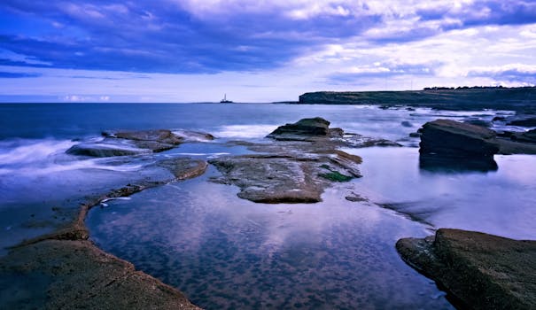 Stunning ocean shore with rocky tide pools, capturing a peaceful evening view under a dramatic sky.