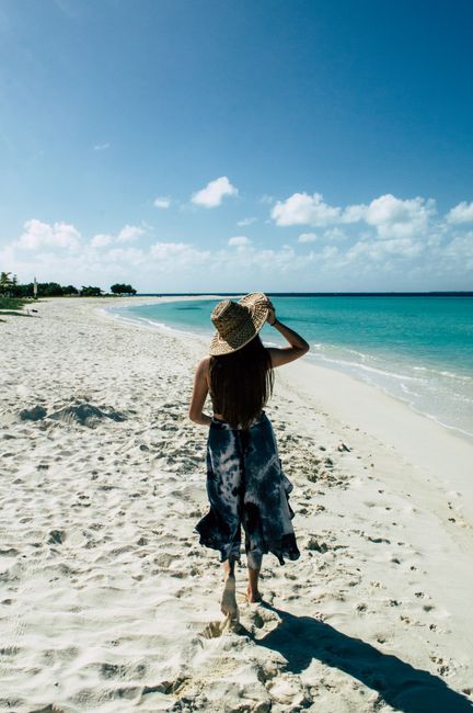 Woman strolling along a tranquil beach in Gran Roque, Venezuela under a clear blue sky.