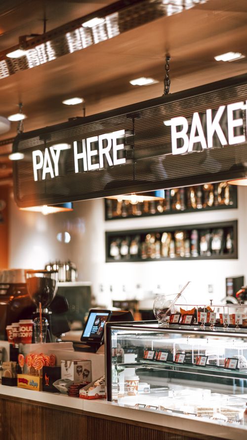 Free Elegant bakery interior showing payment counter and display fridge under bright signs. Stock Photo