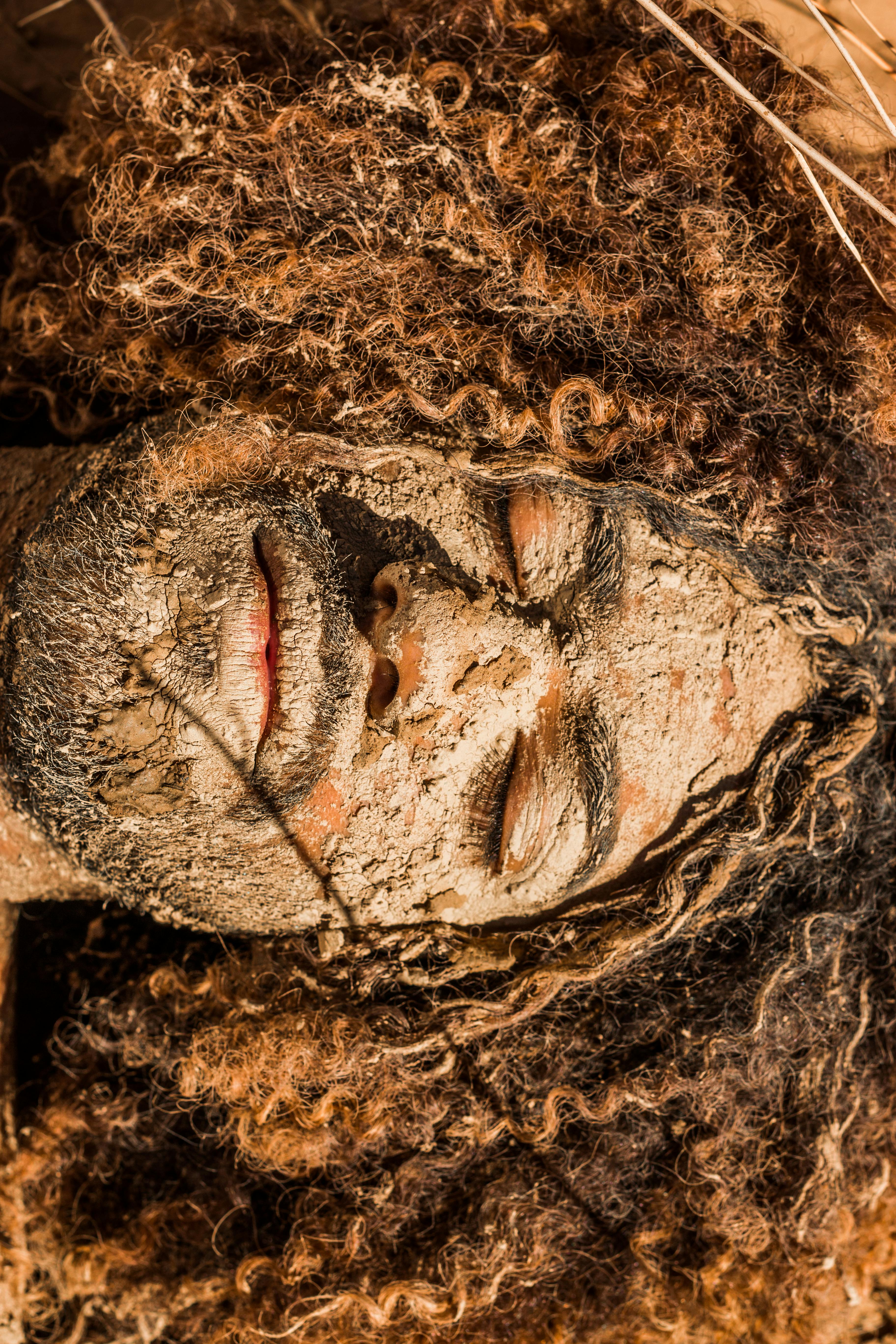 Top view of clayed face of ethnic man with curly hair lying with eyes closed at sunlight