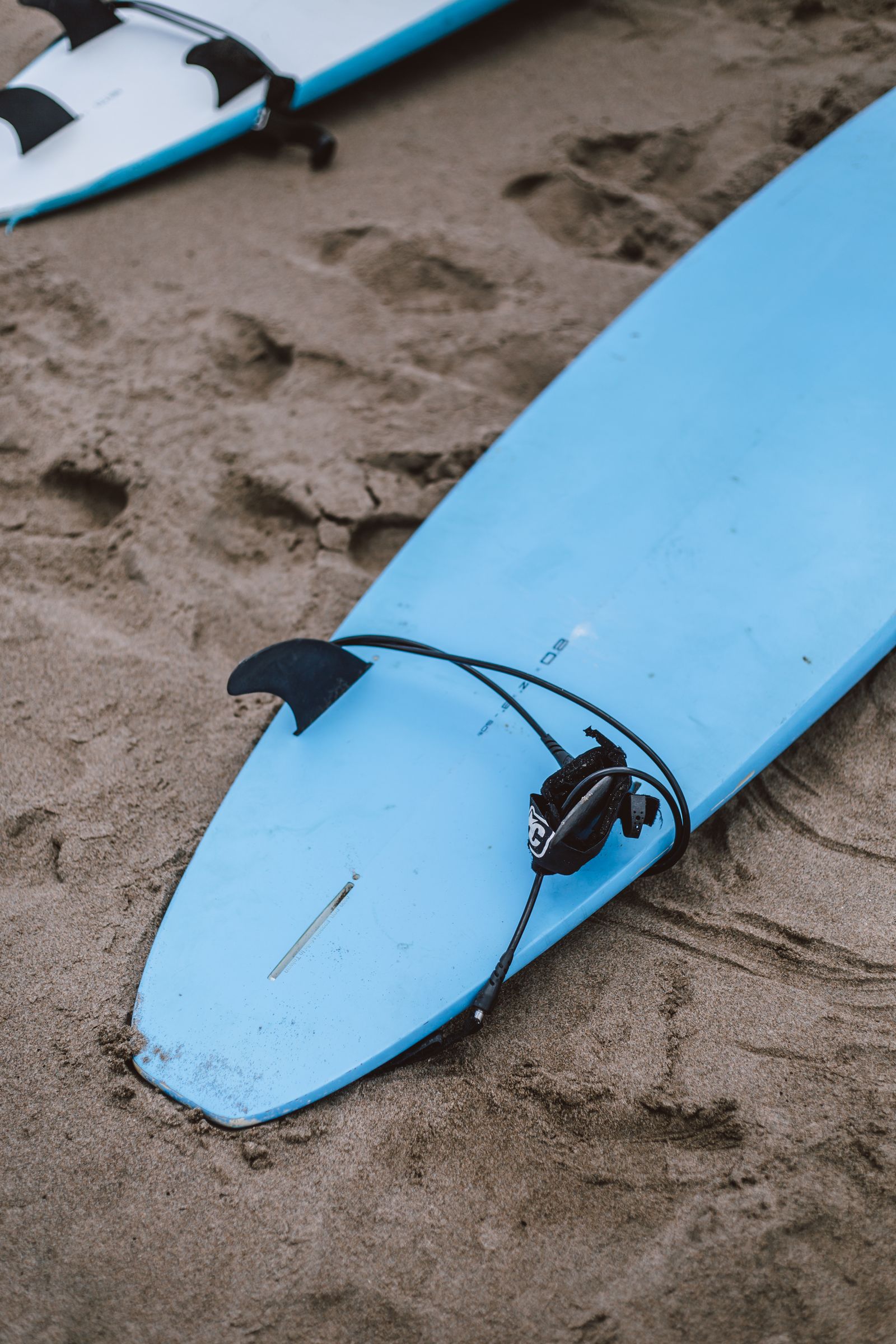 A blue surfboard and its leash resting on sand