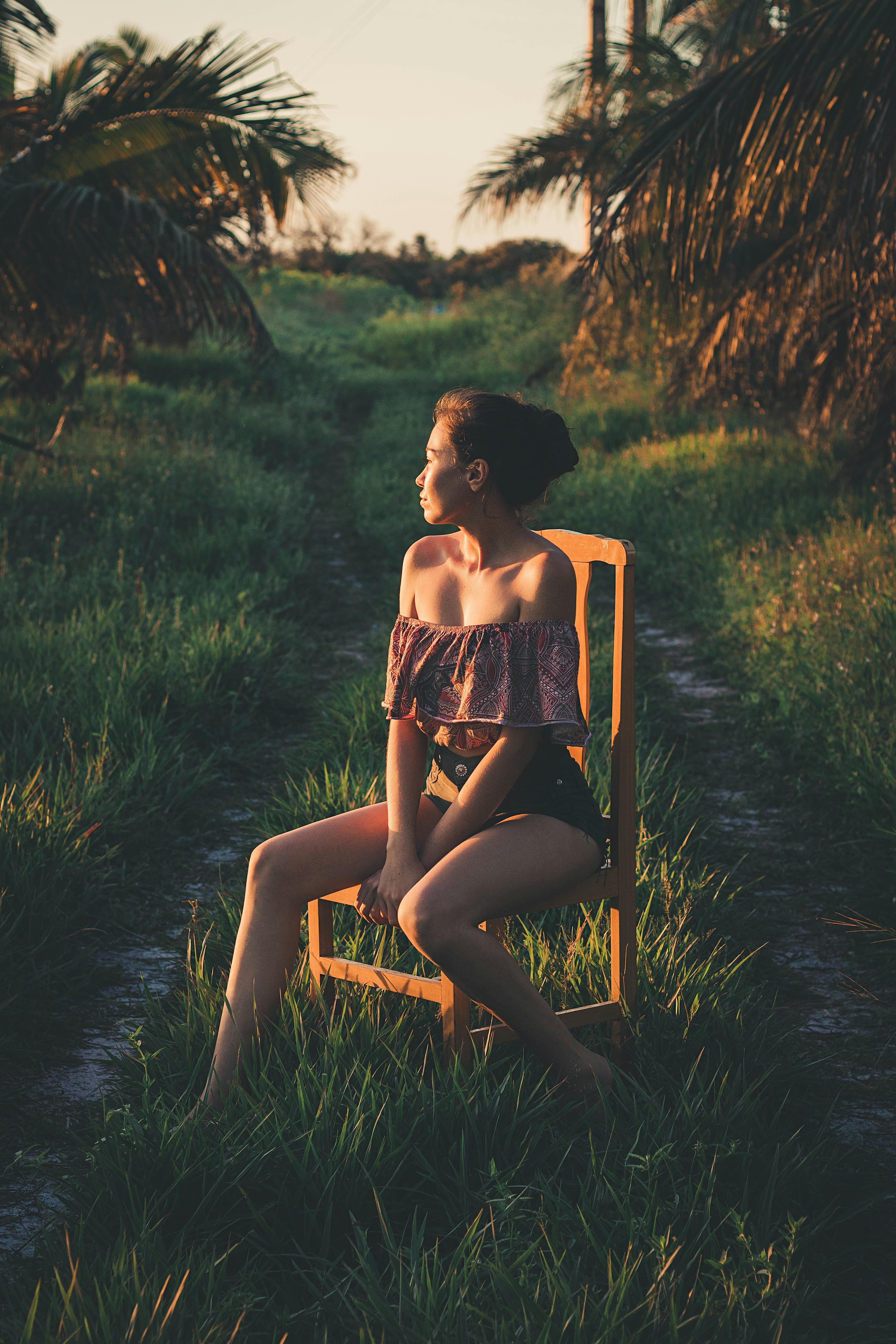 日落时分，一位妇女坐在户外的木椅上，四周环绕着郁郁葱葱的绿植