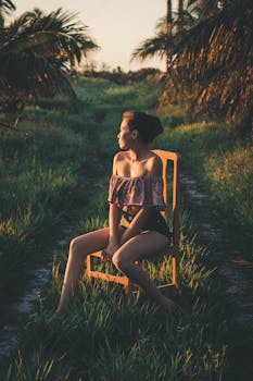 日落时分，一位妇女坐在户外的木椅上，四周环绕着郁郁葱葱的绿植