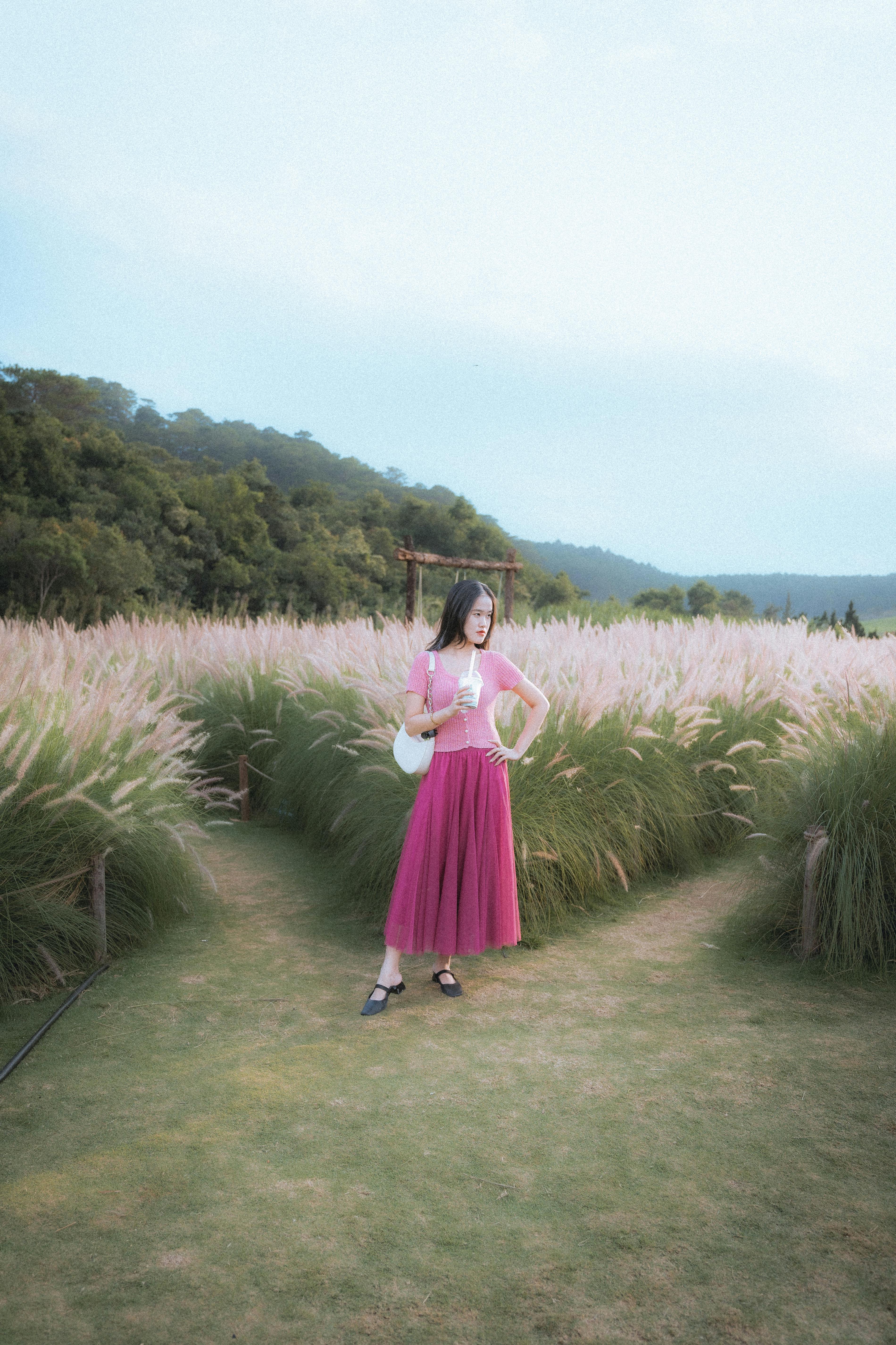 A stylish woman in a vibrant dress poses in a scenic field in Dalat, Vietnam.