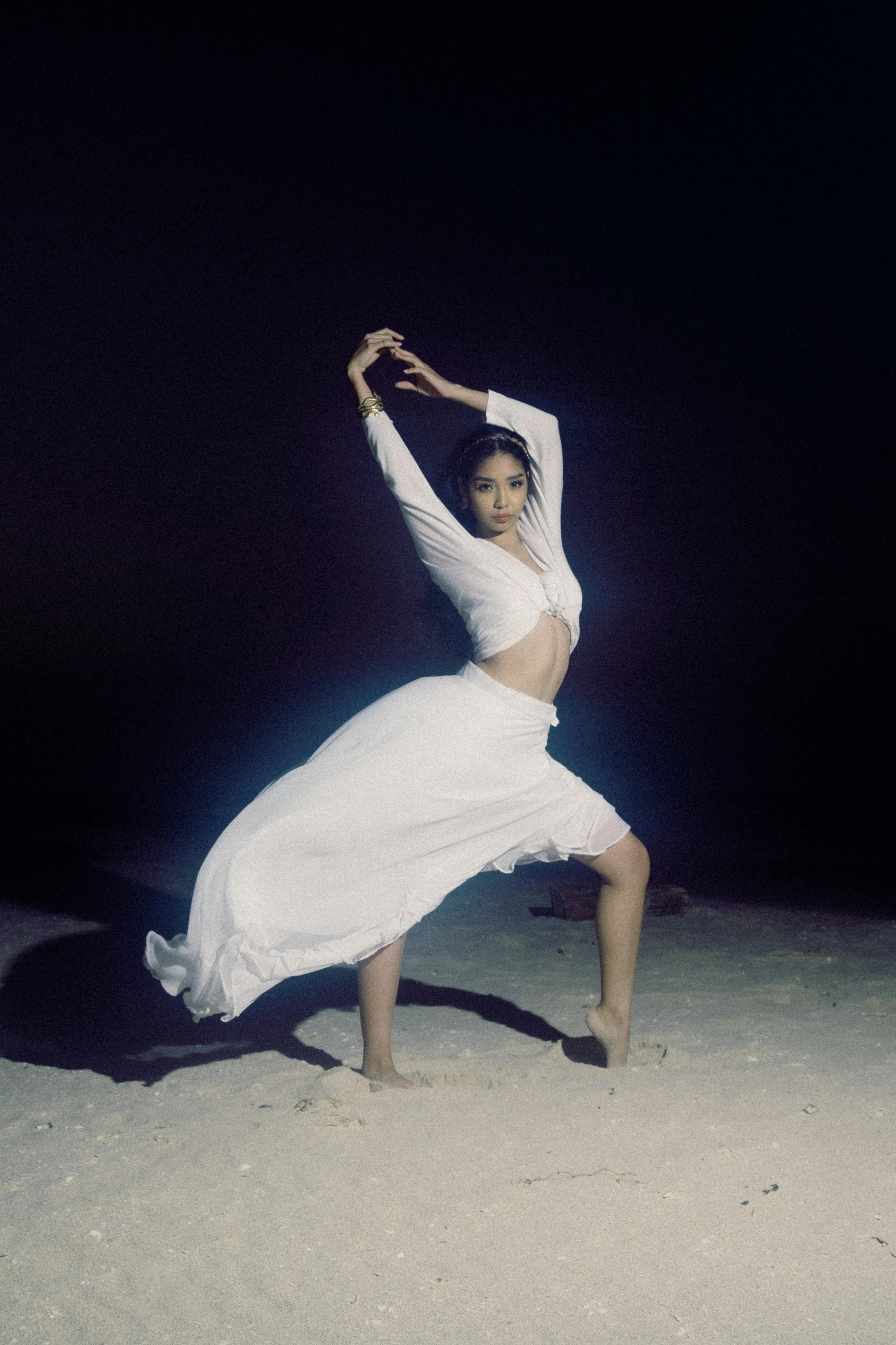 A woman in a white dress striking a pose during a nighttime beach dance performance.