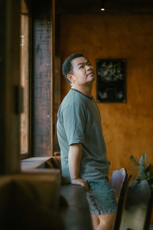 Free Casually dressed man stands by a window in a Ho Chi Minh City café, Vietnam. Stock Photo