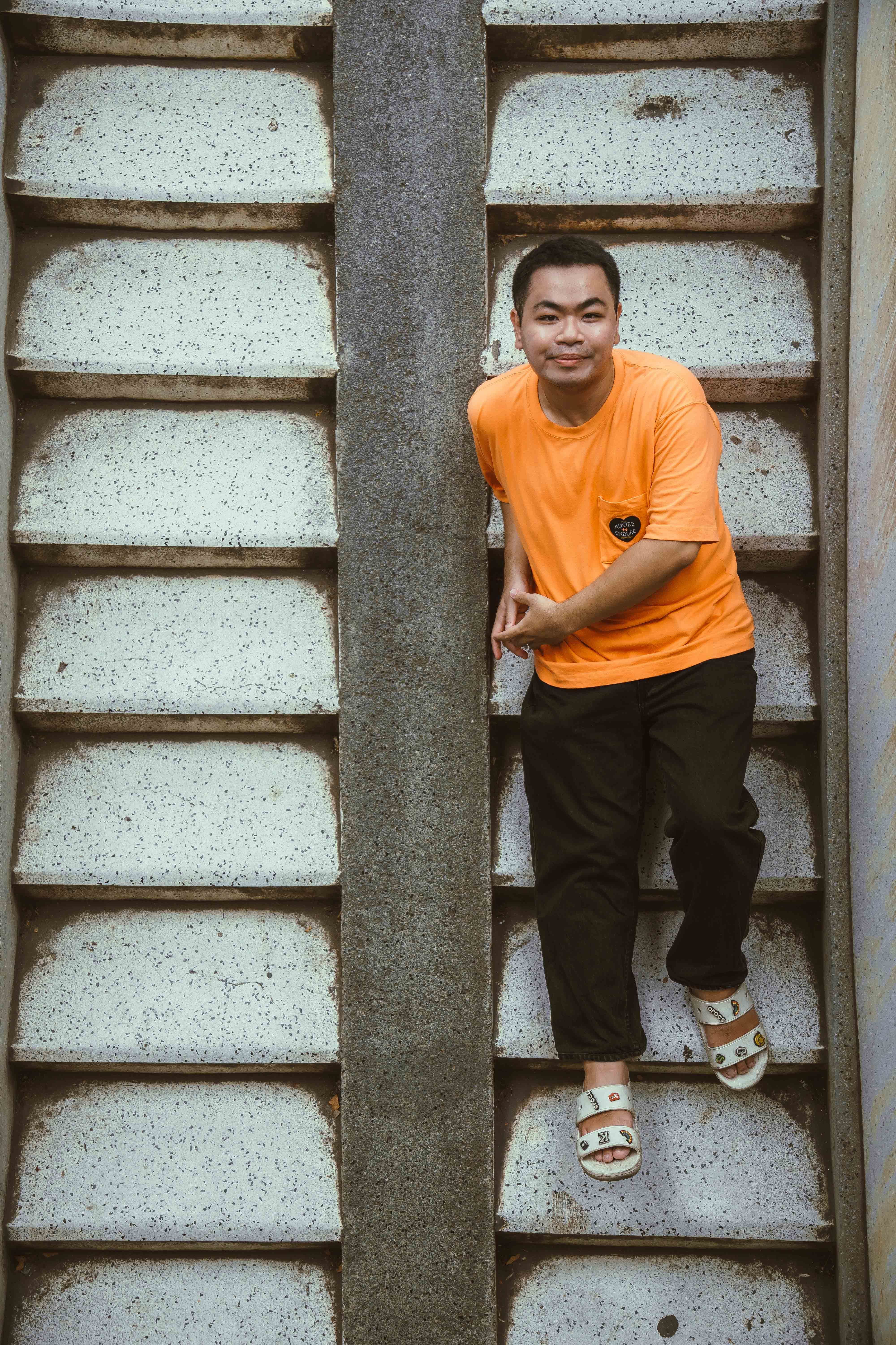 A man in an orange shirt lies casually on concrete stairs in Ho Chi Minh City, Vietnam.