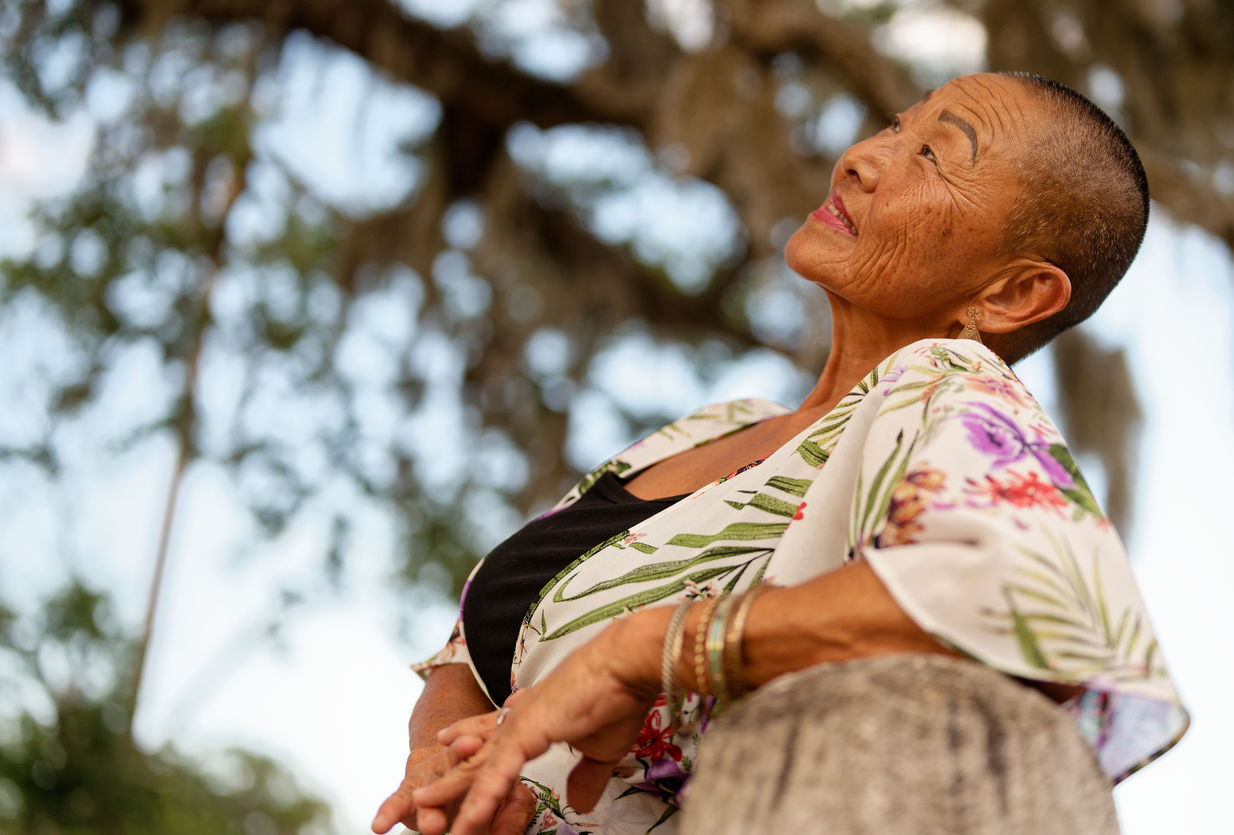 Elderly woman smiling serenely while appreciating the beauty of nature outdoors.
