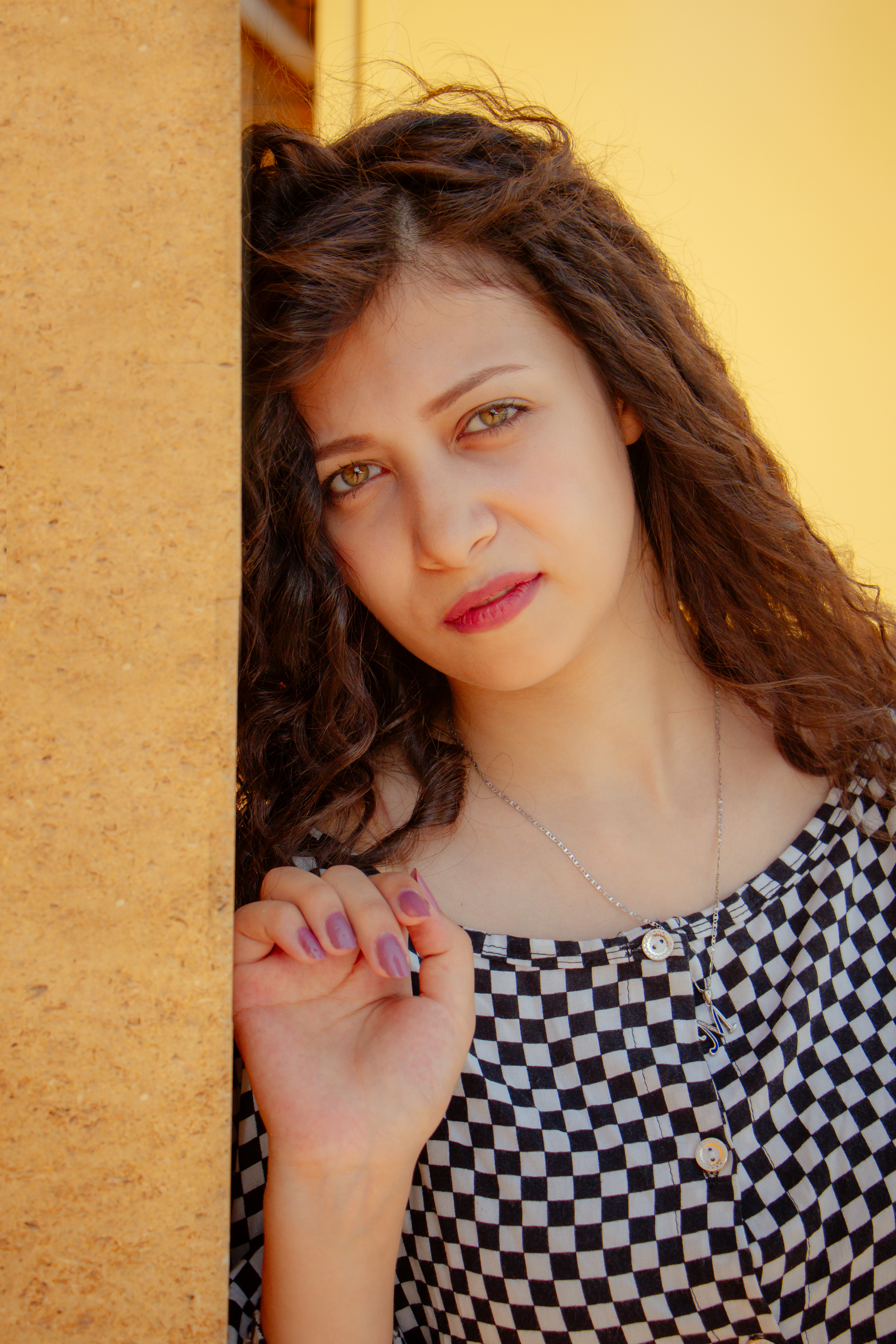 Beautiful young woman posing in a checkered dress against a warm backdrop in Cairo, Egypt.