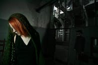 一位红发女子在光线昏暗的工业室内沉思伫立