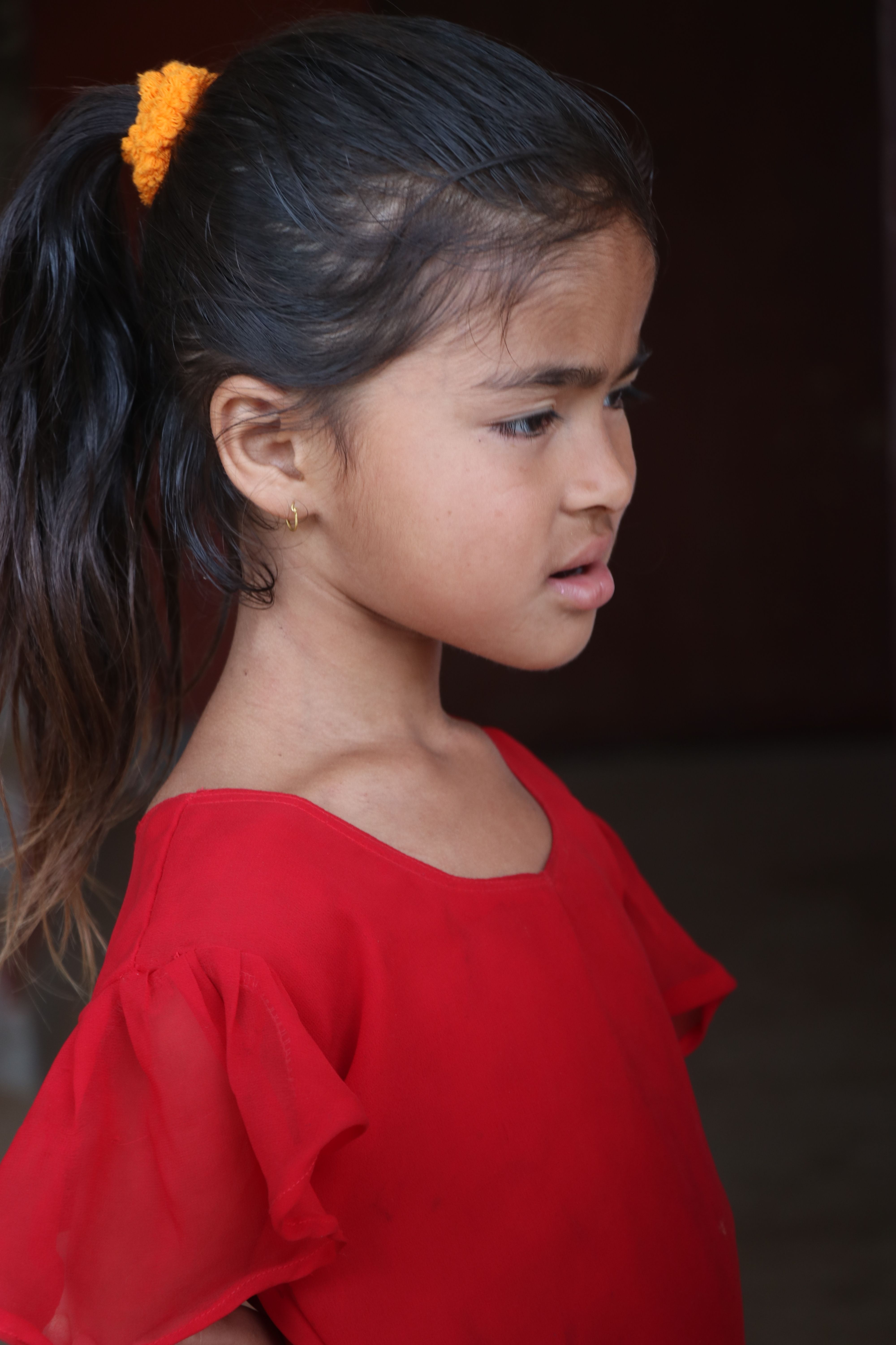 Portrait of a young girl in a red dress, wearing a yellow hair tie and earring.