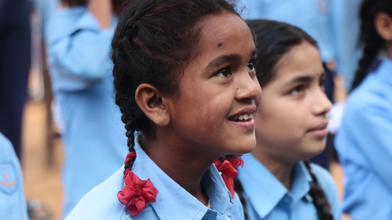 A group of smiling schoolchildren in uniform at an outdoor school gathering in South Asia