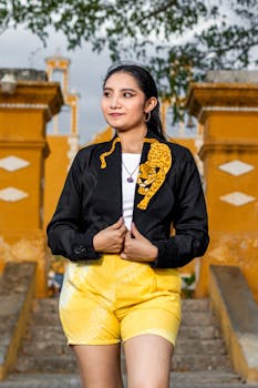 Stylish woman wearing a black bolero with tiger design and yellow shorts, standing outdoors.