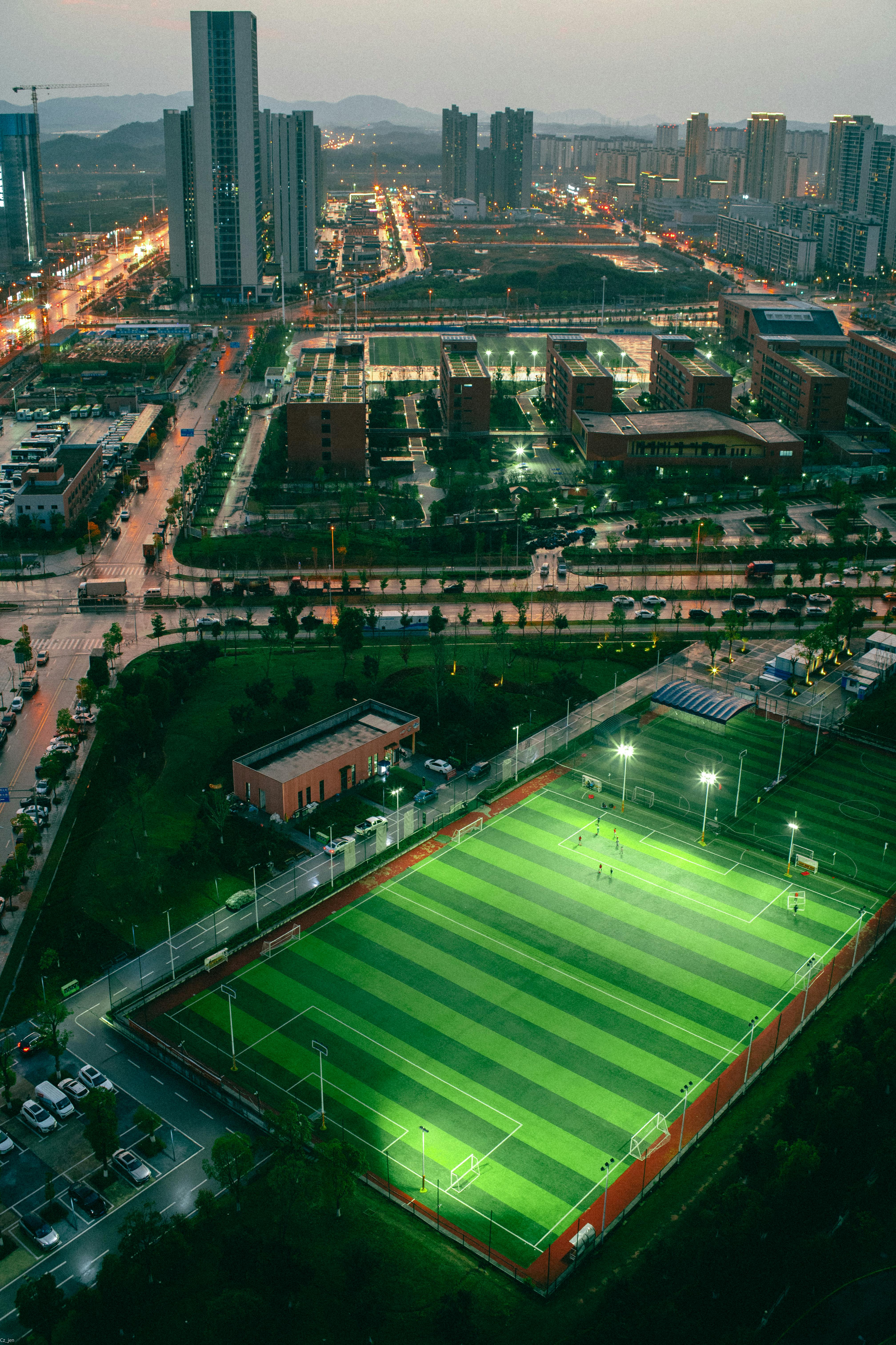 A vibrant cityscape showcasing an illuminated soccer field amidst towering buildings at dusk.