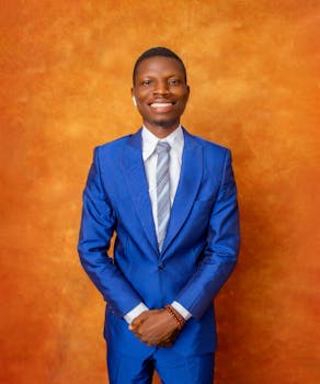 A smiling man in a blue suit posing elegantly in a studio setting.