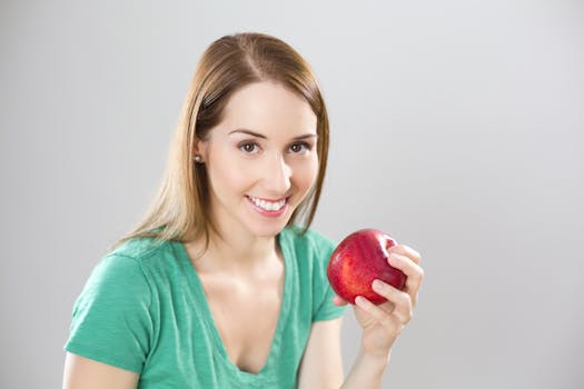Portrait of Young Woman Eating Fruit Against White Background