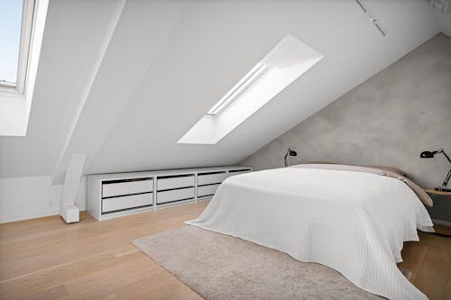 A bedroom with a white bed and a skylight