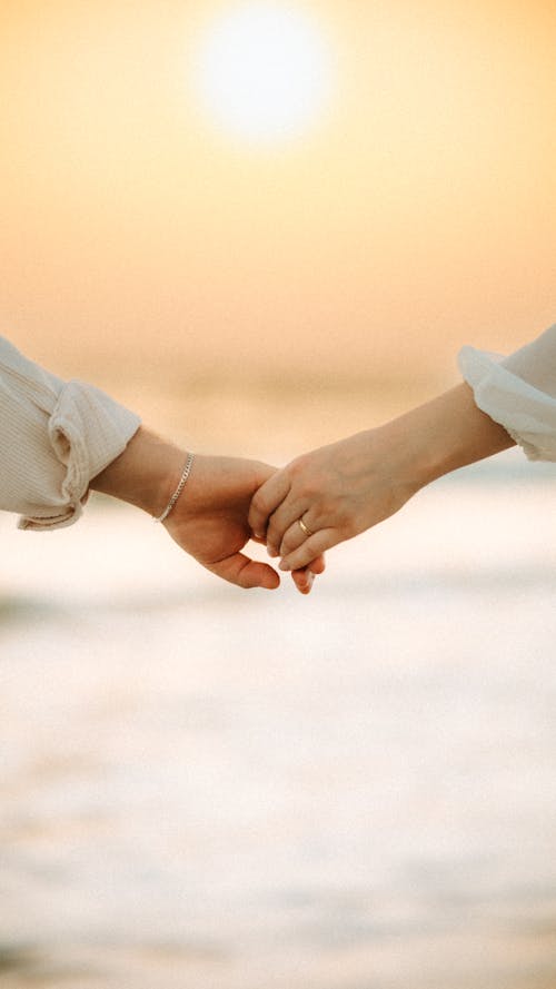 Two people holding hands on the beach at sunset