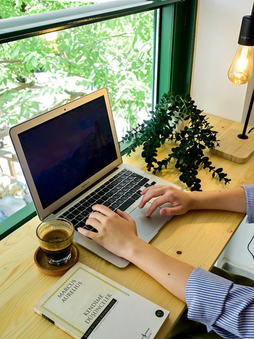 Free Tranquil workspace with laptop, coffee, and plant by a sunlit window. Stock Photo