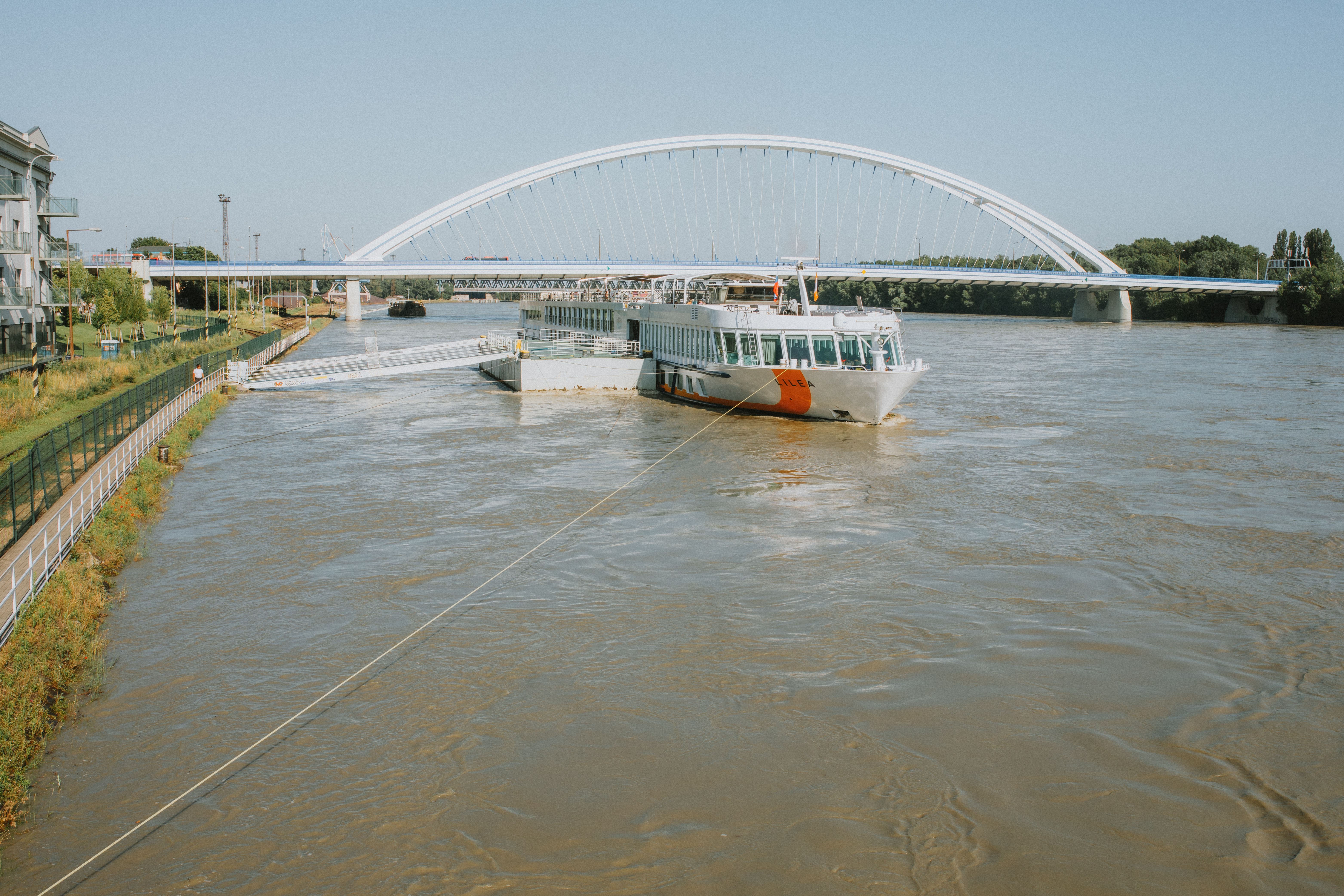 A scenic view of a bridge spanning a river with a moored ferry, under a bright sky.