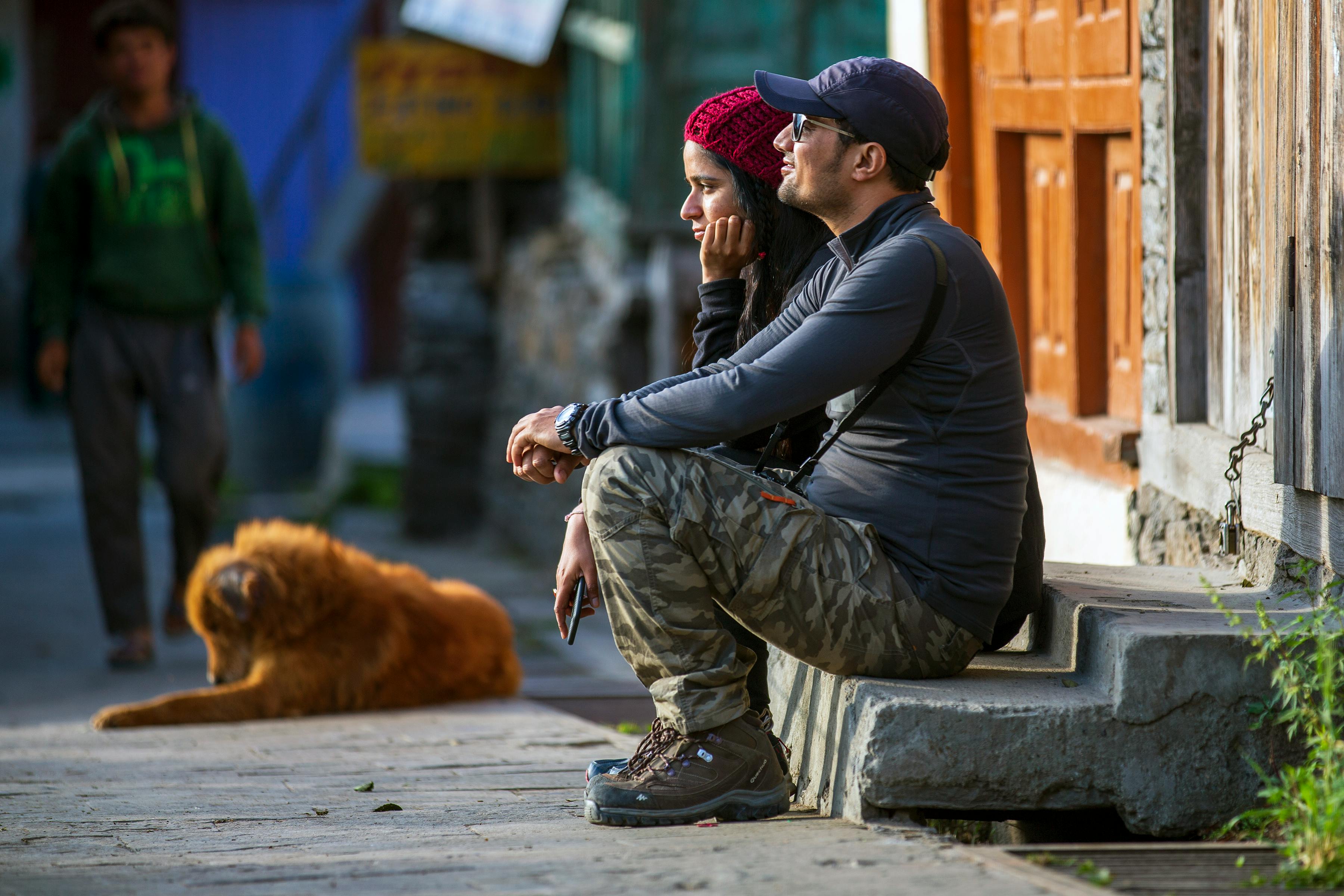 一对夫妇坐在街边的台阶上，旁边有只狗，正观察着周围的环境