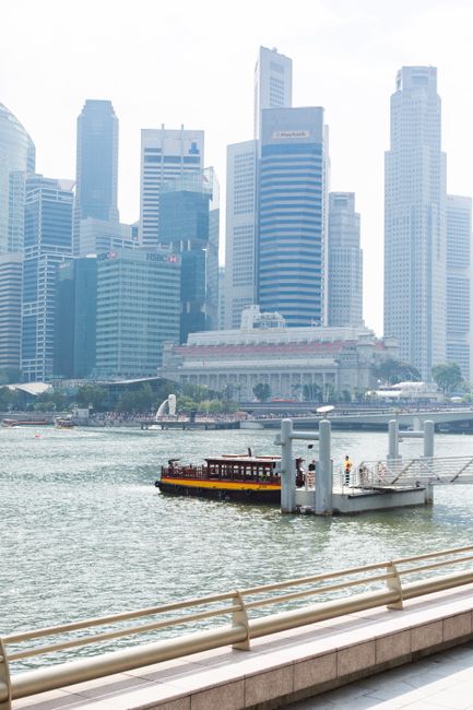 View of Singapore's modern skyline with a ferry on calm waters under a clear sky.