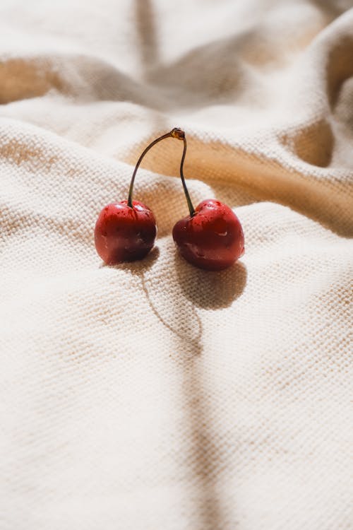 Two cherries on a white cloth with a shadow