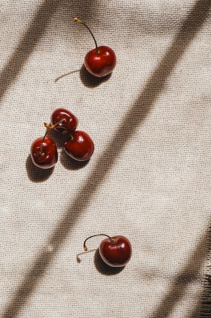 Vibrant red cherries scattered on a light textured cloth, creating a rustic and artistic still life composition.