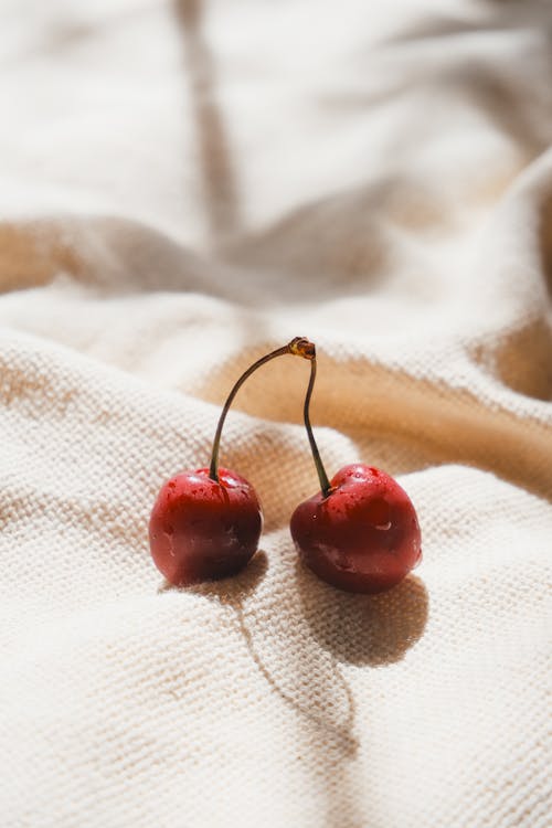 Two cherries on a white cloth with a white background