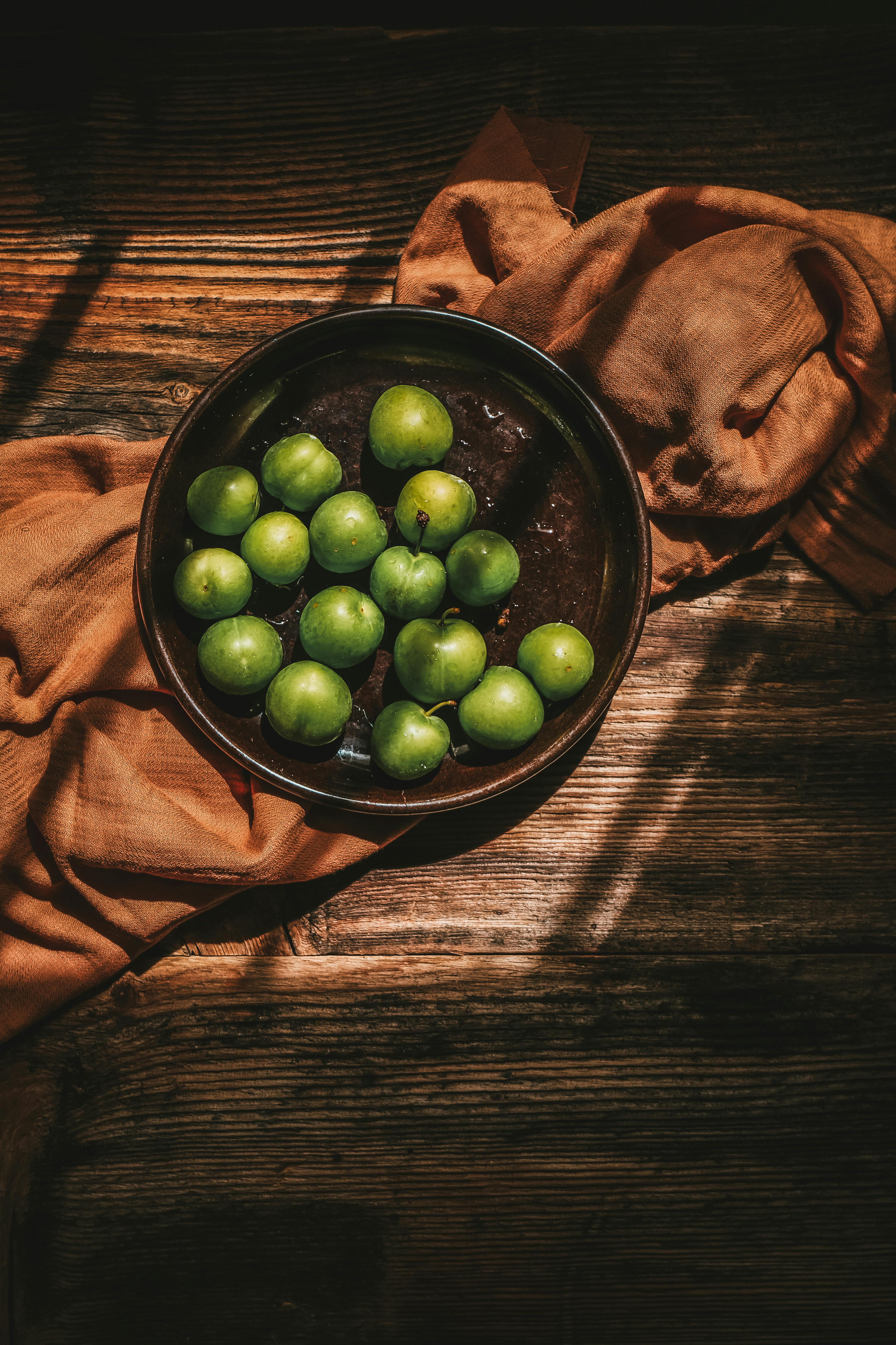 A rustic still life composition featuring green apples in a wooden bowl on textured surface.