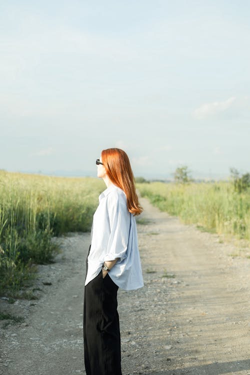 A woman with red hair stands on a dirt road