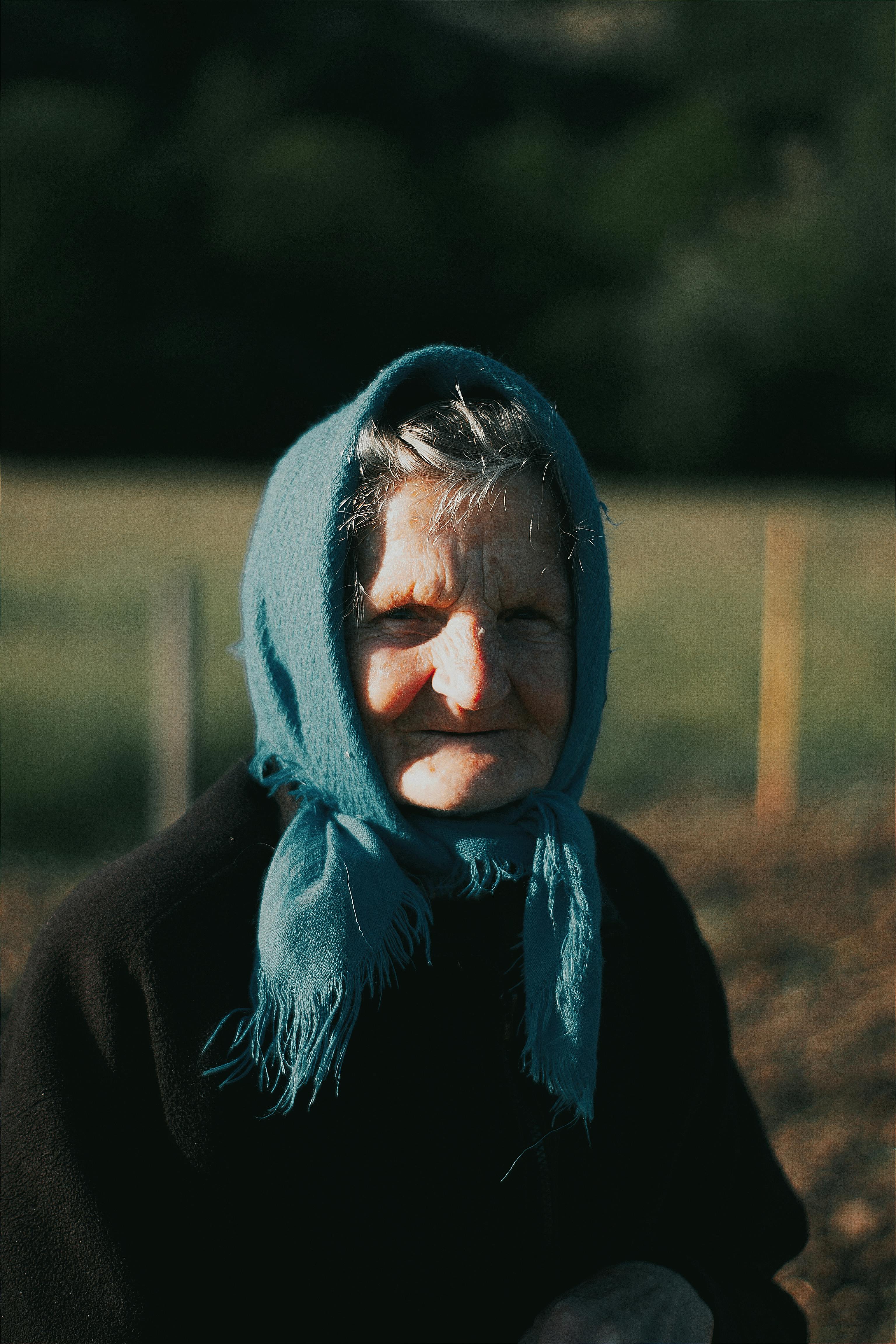 Portrait of a senior woman with a blue headscarf in a rural setting in Hungary.