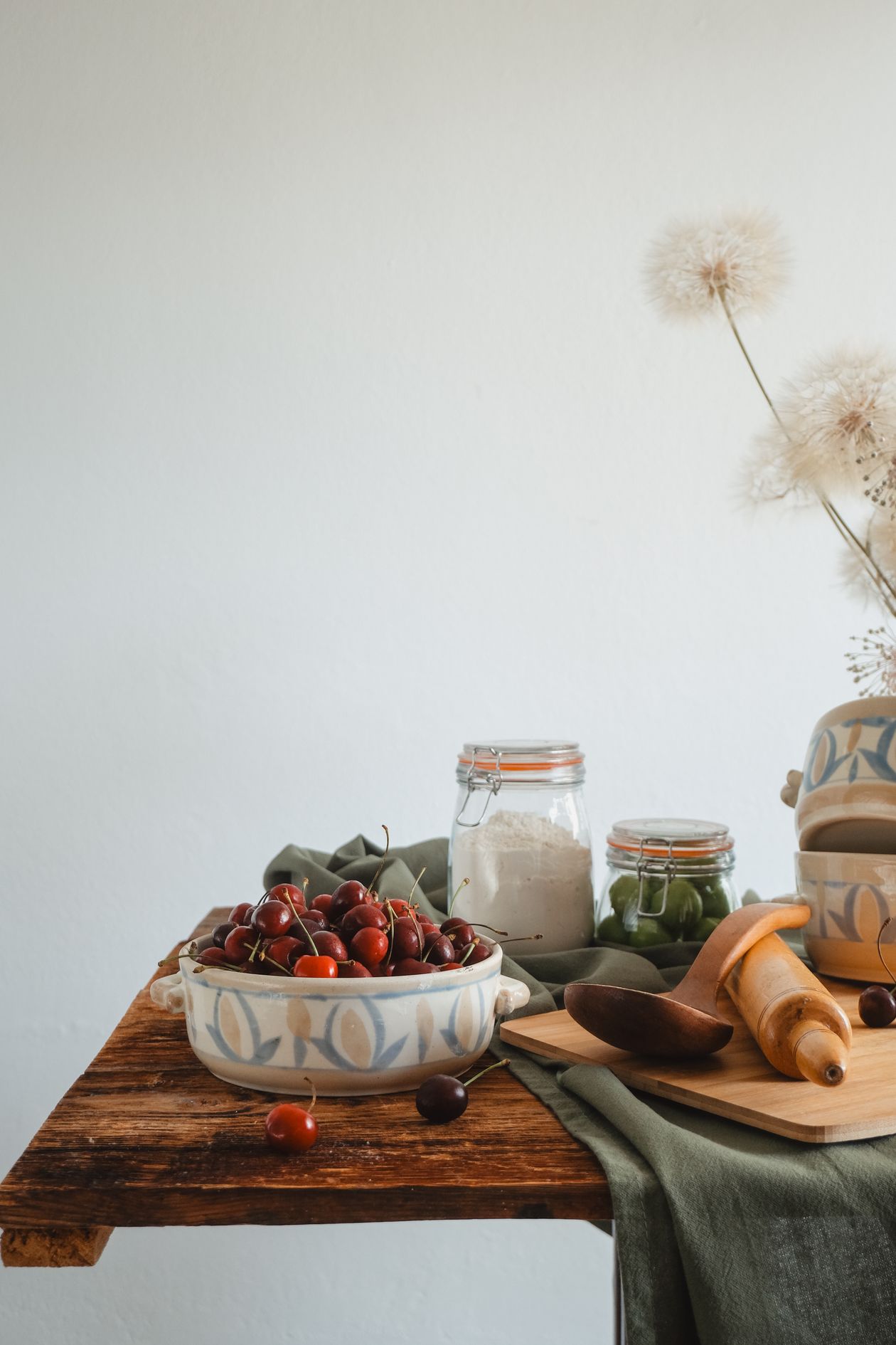 Cherries, jars and wooden utensils styled on a table Bowl of cherries with glass jars and wooden utensils on a rustic table