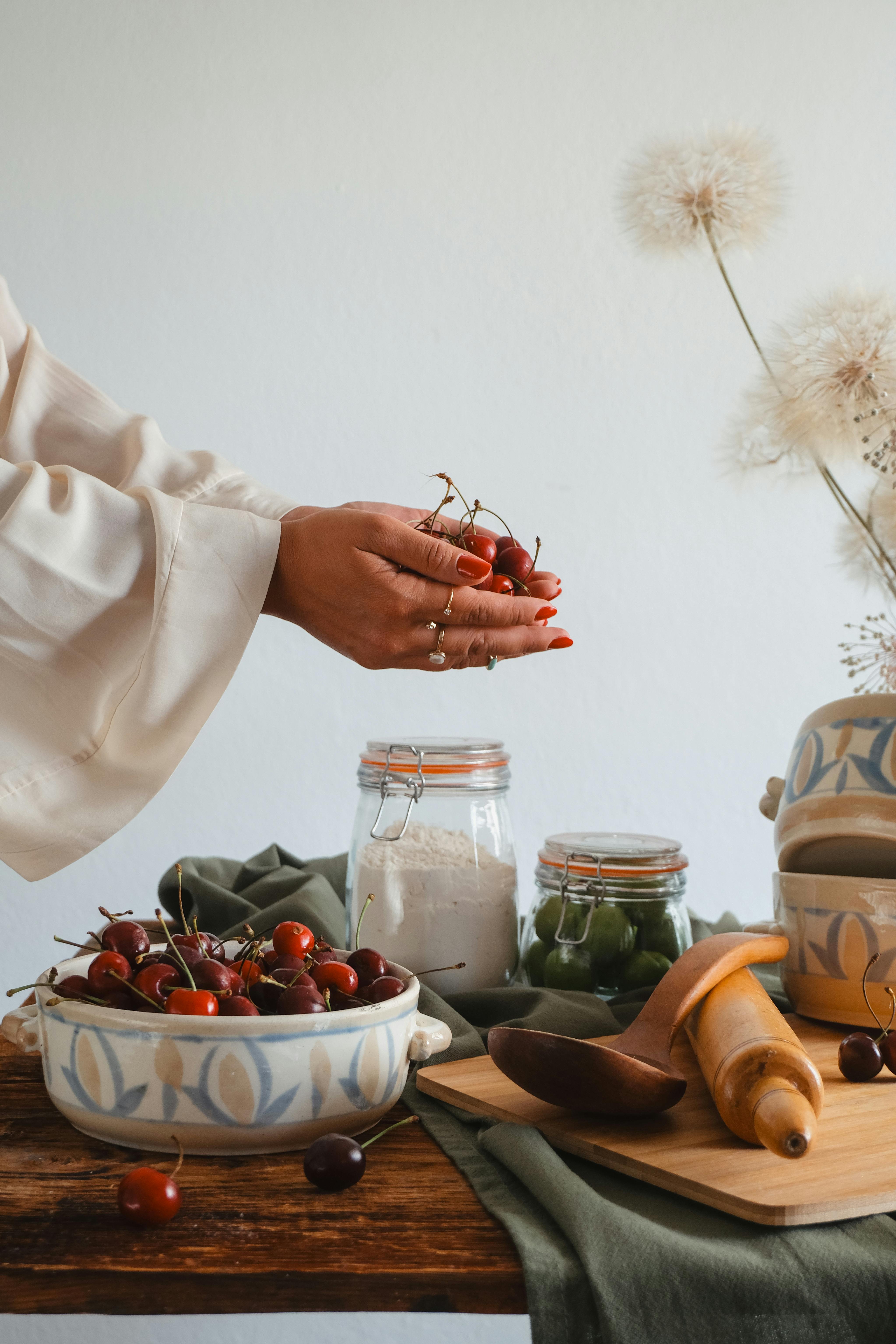 A woman holds fresh cherries in a rustic kitchen with baking supplies around.